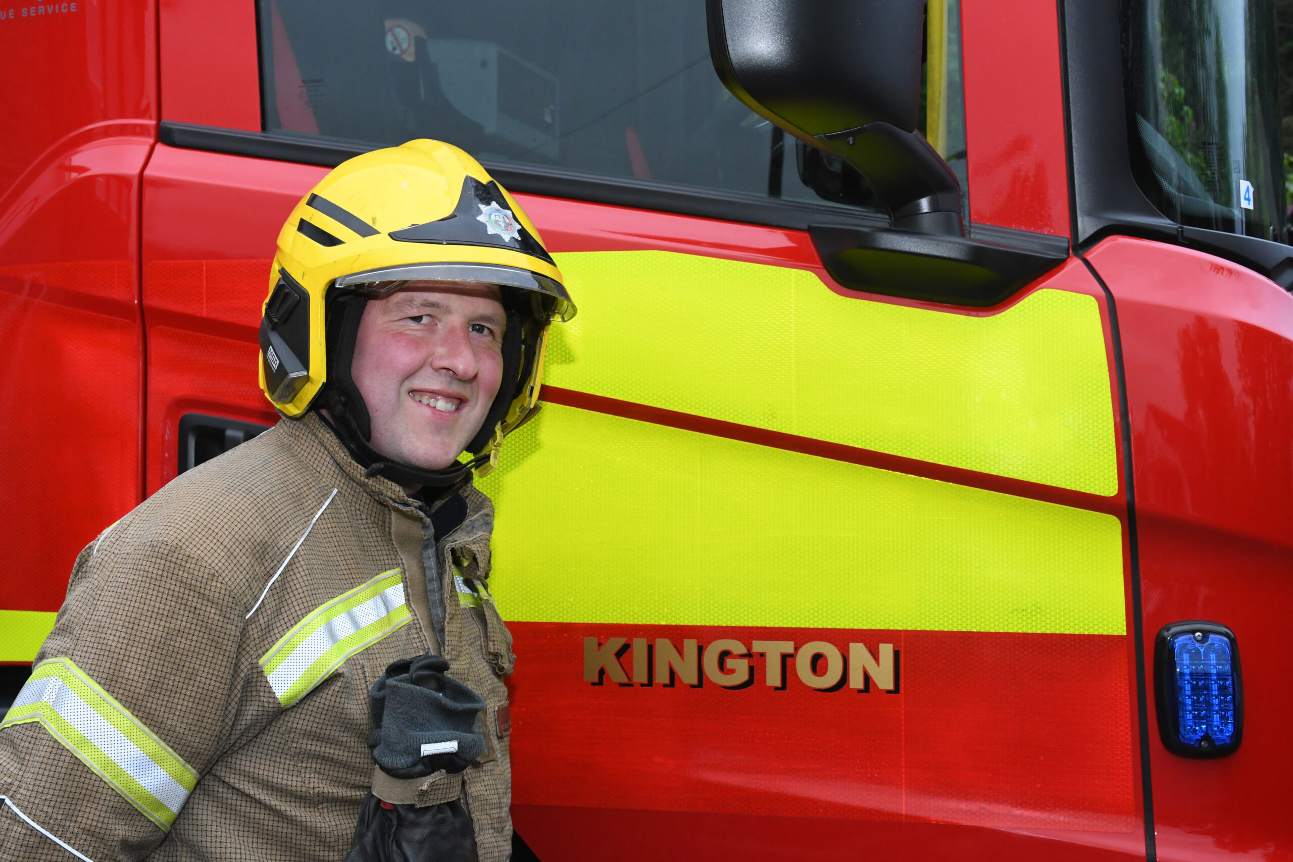 An on call firefighter standing in front of fire engine smiling
