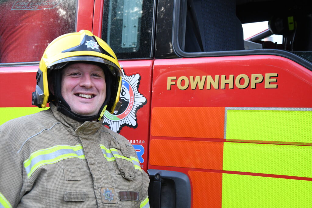 Firefighter wearing yellow helmet standing in front of a fire engine from Fownhope