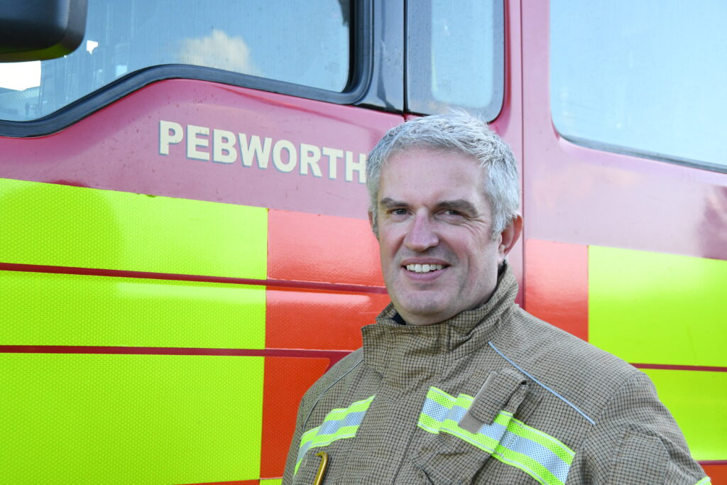 Firefighter in fire kit standing in front of Pebworth fire engine